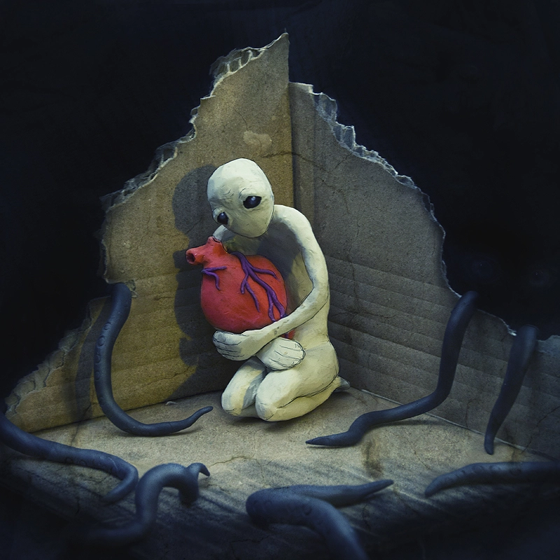 Little sculpture holding tight a huge realistic anatomic heart - defending it from tentacles reaching for him out of the dark